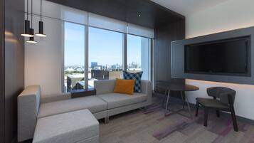 A modern living room with a large TV, a sofa, a coffee table, and a view of the city.