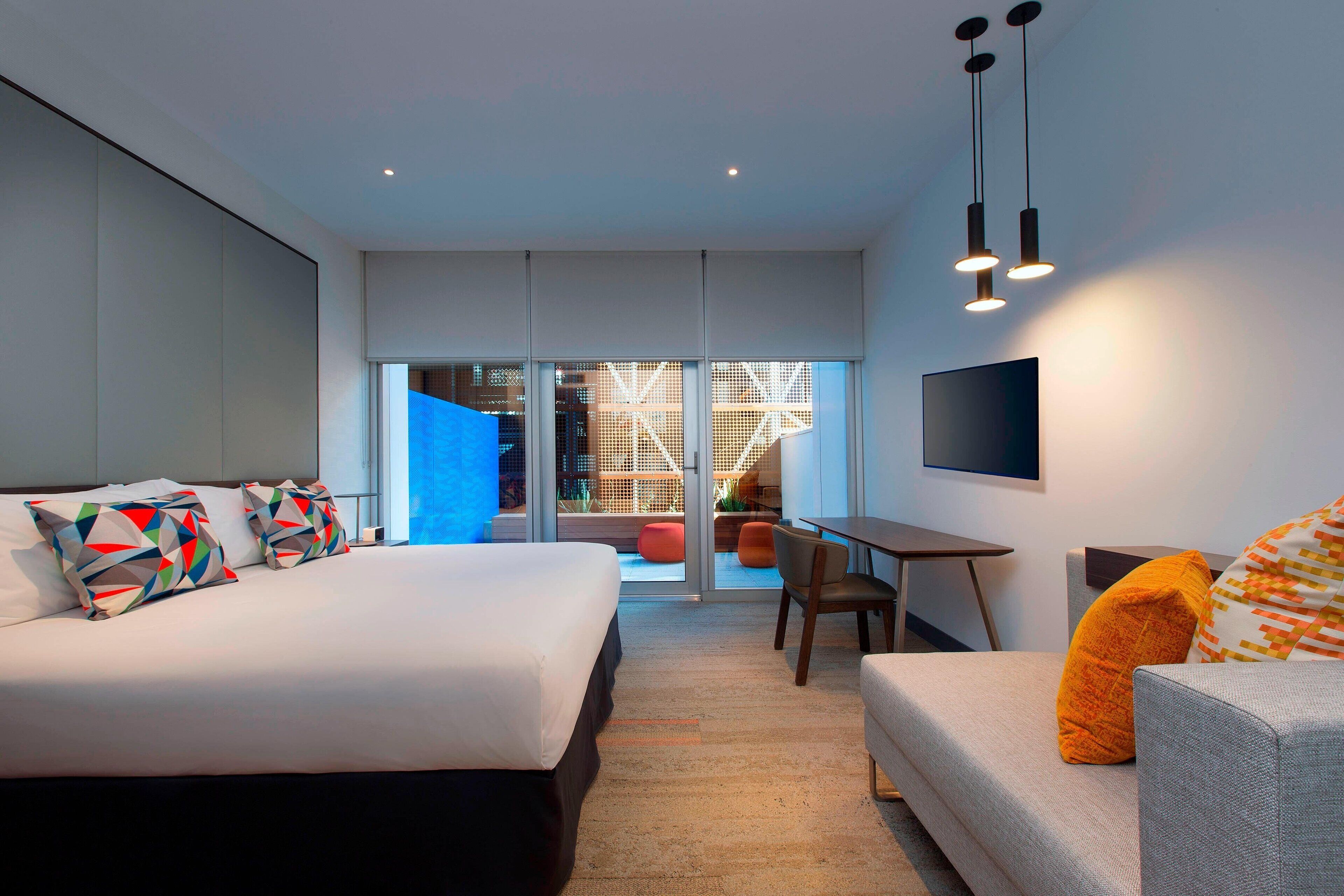 Une chambre d’hôtel moderne équipée d’un grand lit, d’un canapé, d’un bureau et d’un téléviseur fixé au mur.