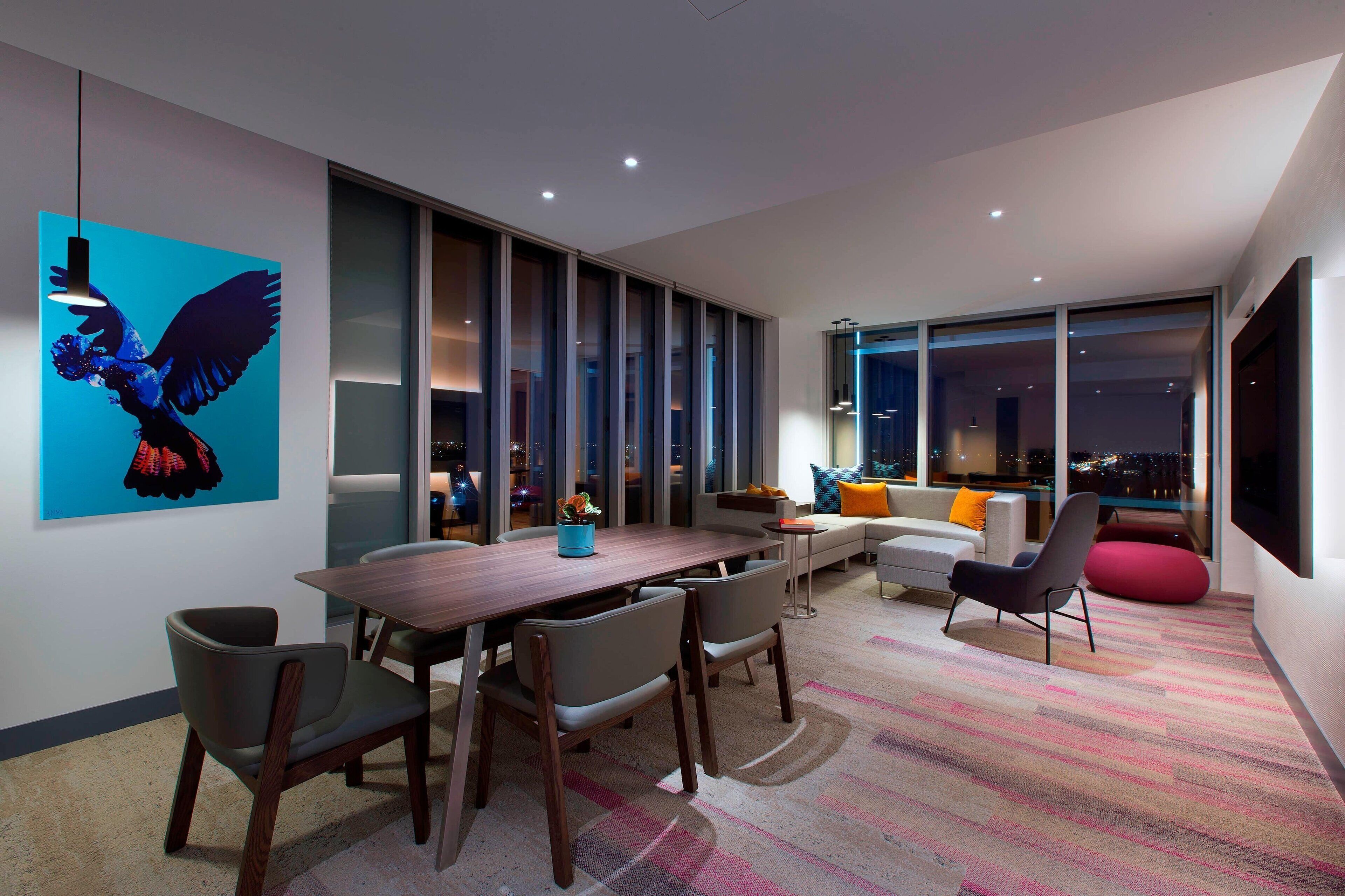 A modern interior with a dining area, sofas, and a large window offering a city view.
