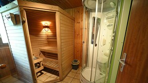 Een houten sauna met een bank en een doucheruimte met glazen wanden.