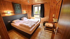 Een houten slaapkamer met twee bedden, een raam met gordijnen, een wastafel en een wandlamp.