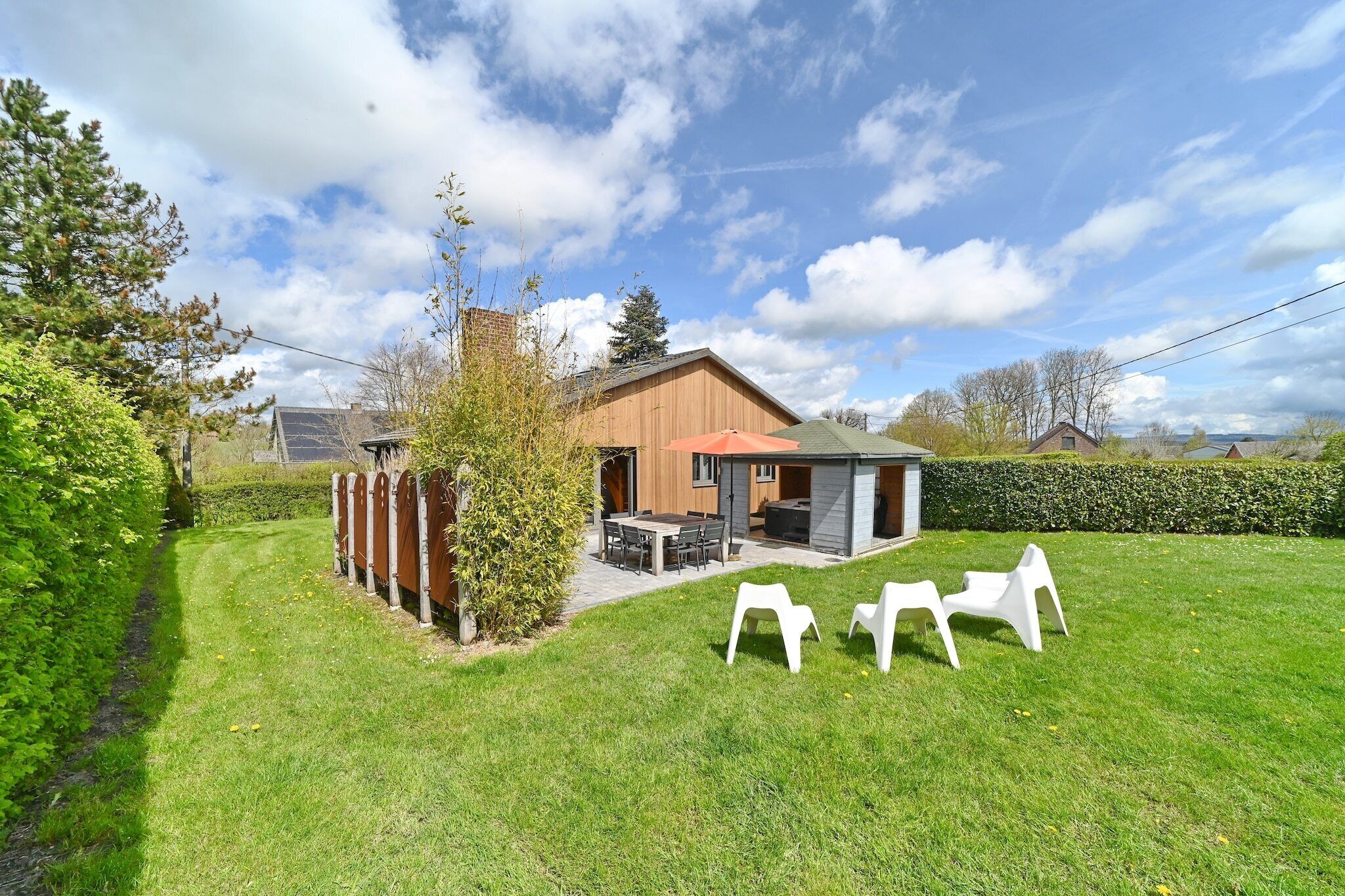 Een modern huis met een houten gevel, een terras met tuinmeubilair en een verzorgd gazon.