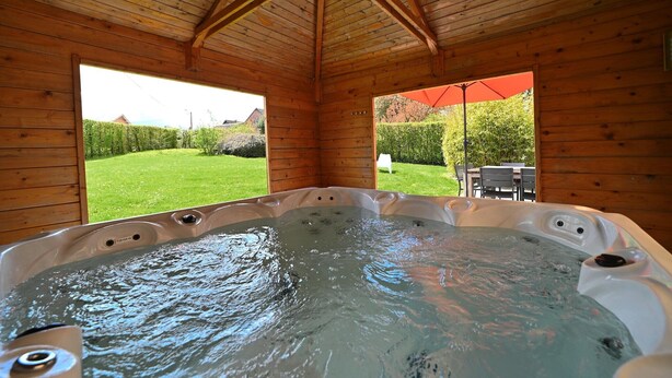 Een houten hut met een jacuzzi en uitzicht op een groen gazon en bomen.