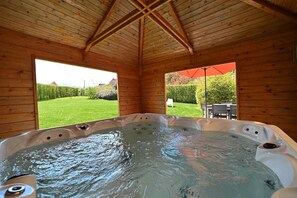 Uma cabana de madeira com hidromassagem e vista para um gramado verde e árvores.