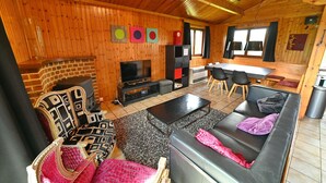 Een knus blokhutinterieur met een open haard, houten wanden, een televisie en een eethoek.