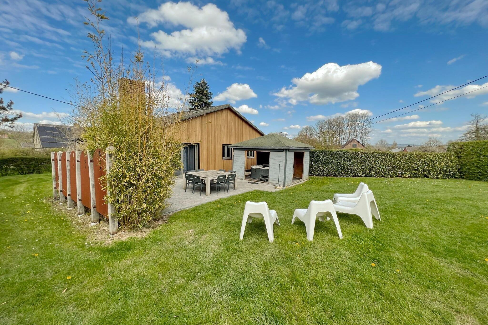 Une maison moderne avec une façade en bois, une terrasse avec une table et des chaises, et un petit abri de jardin.