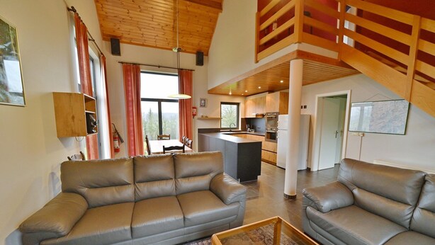 A spacious living area with a large leather sofa, a wooden coffee table, and a kitchen in the background.