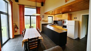 A spacious kitchen with a dining area, wooden ceiling, and large windows.