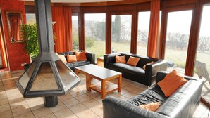 Ein Wohnzimmer mit Kamin, zwei Sofas, einem Couchtisch und großen Fenstern mit Vorhängen.