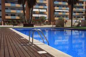 A swimming pool with a wooden deck, surrounded by a multi-story building with balconies. - Suitur Barcelona  Olympic (Barcelona)