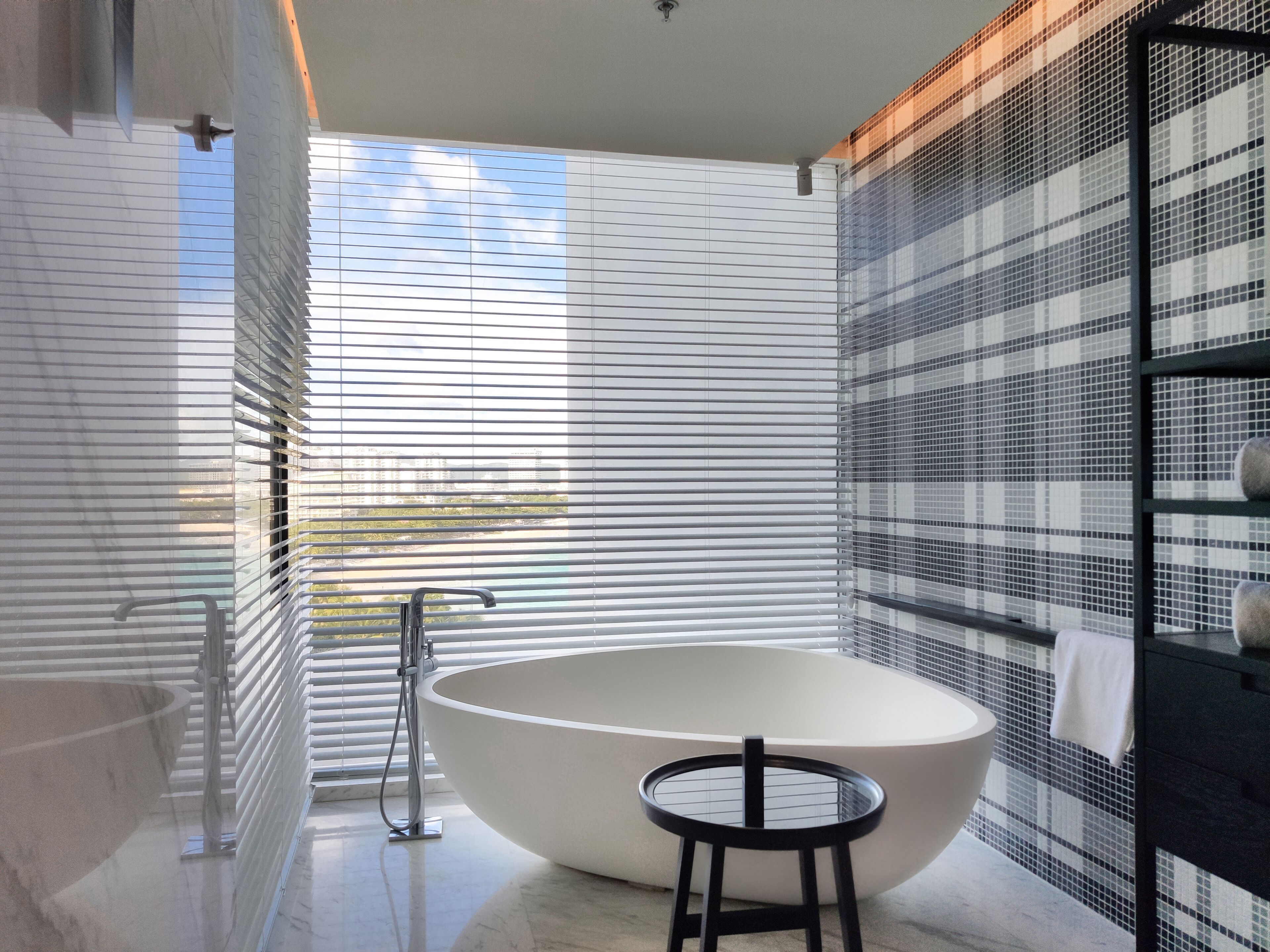Une salle de bain moderne avec une baignoire sur pieds, un petit tabouret et une fenêtre avec des stores.