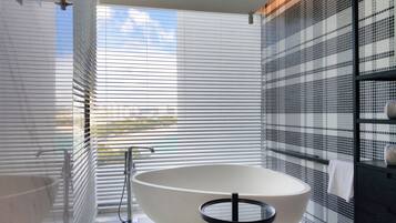 Un bagno moderno con una vasca freestanding, un piccolo sgabello e una finestra con persiane.