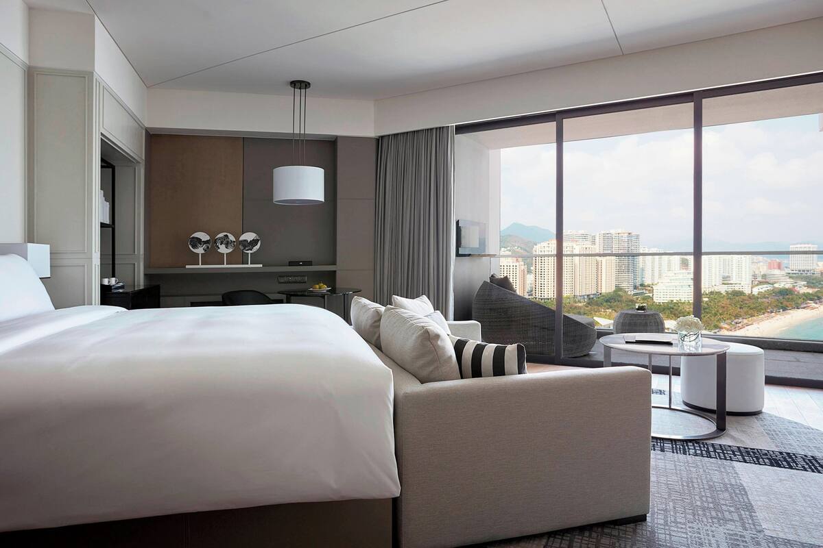 Une chambre d’hôtel moderne dotée d’un grand lit, d’un canapé, d’une petite table ronde et offrant une vue sur le paysage urbain.