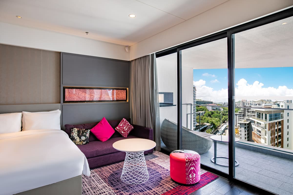 Une chambre d’hôtel moderne dotée d’un grand lit, d’un canapé, d’une petite table ronde et d’un balcon offrant une vue sur la ville.