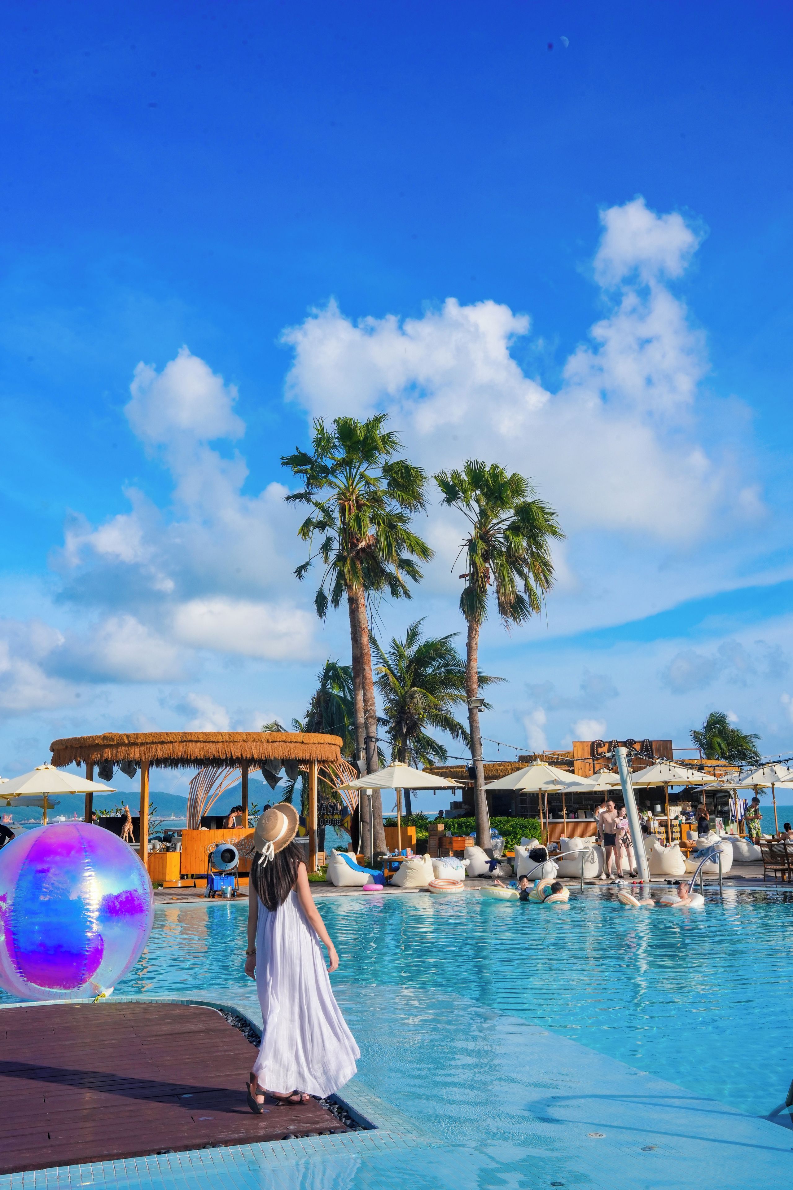 A pool area with a clear sky, palm trees, and lounge chairs.