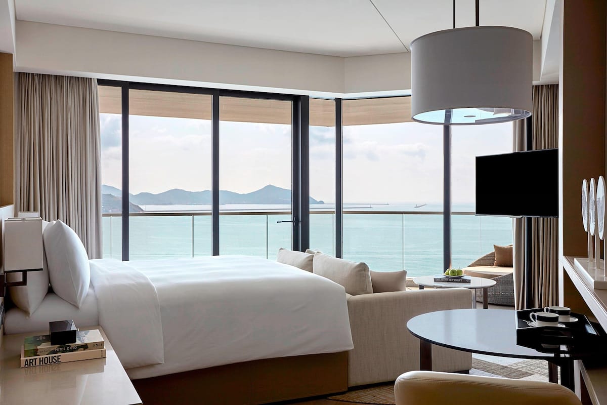 Une chambre d’hôtel avec un grand lit, un canapé, une petite table, une télévision et une vue sur la mer.