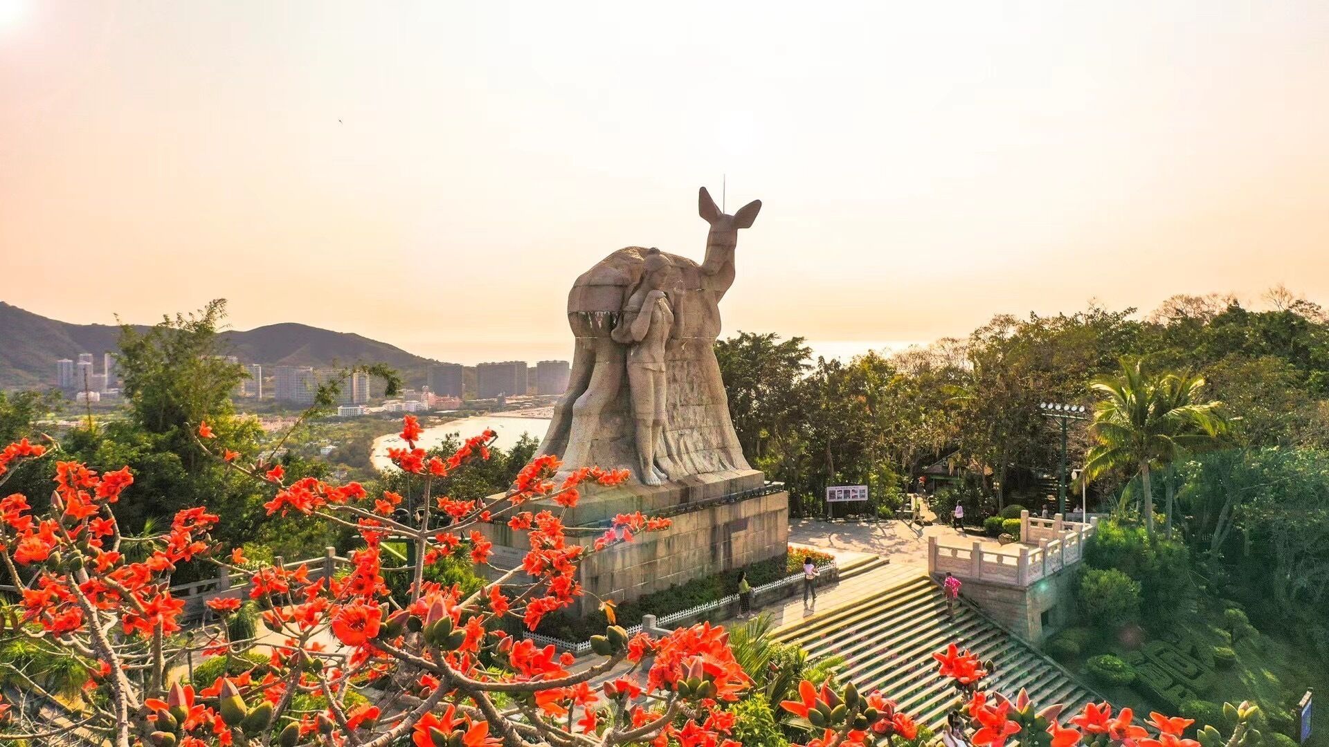 A large stone statue in a park with a view of a river and cityscape in the background.