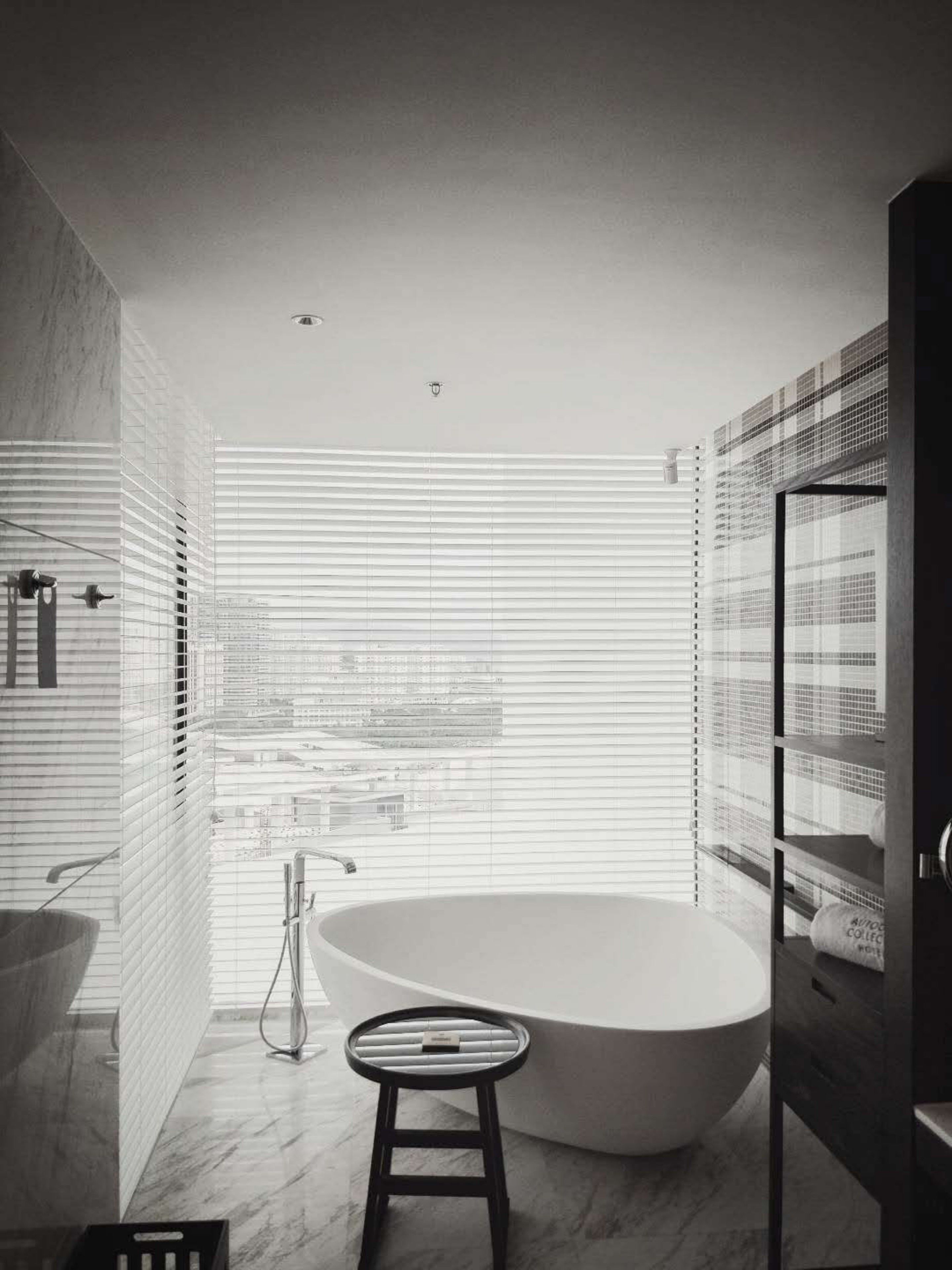 A modern bathroom with a freestanding bathtub, a marble floor, and a view through large windows.