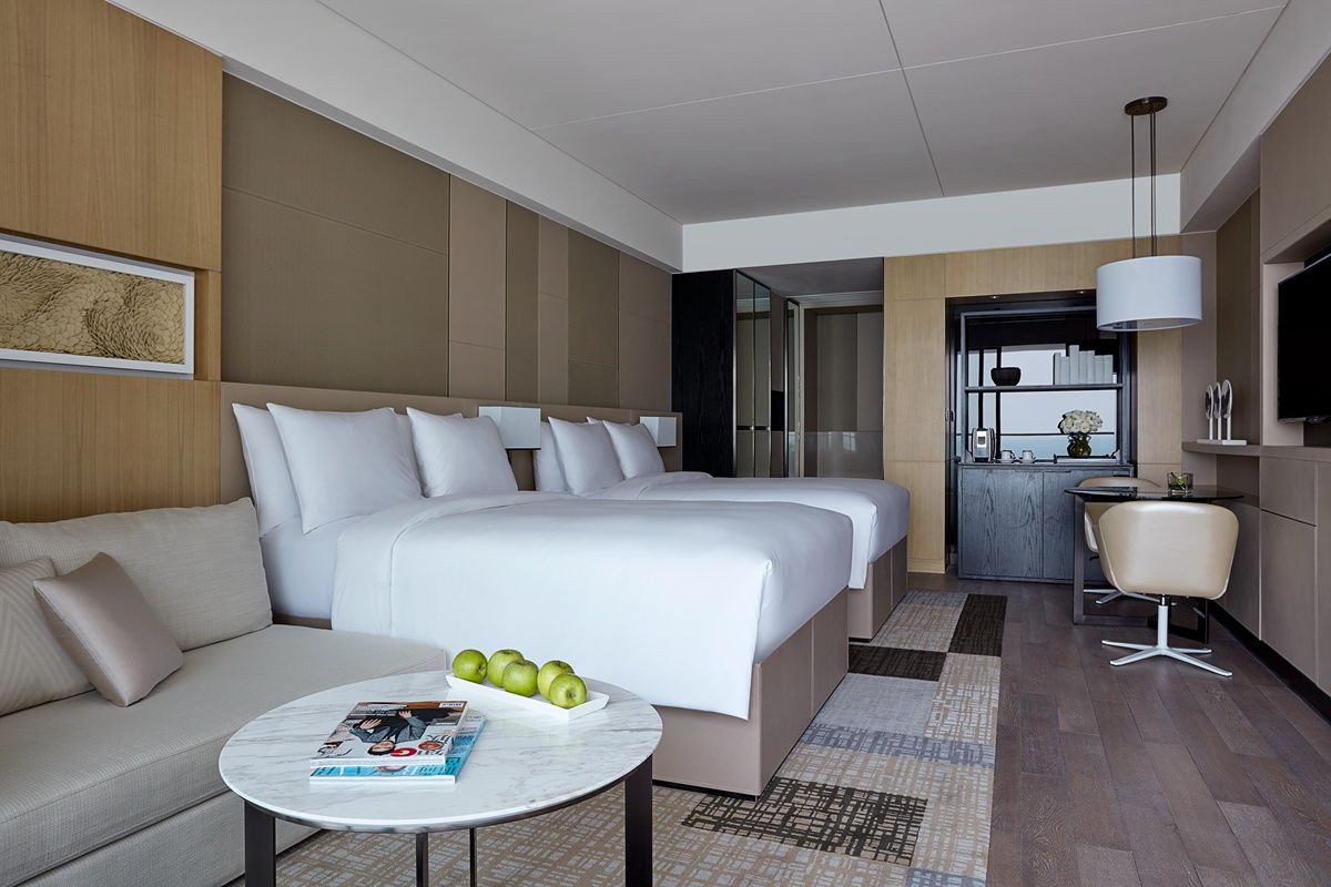 A hotel room with a large bed, a sofa, a dining area, and a TV.