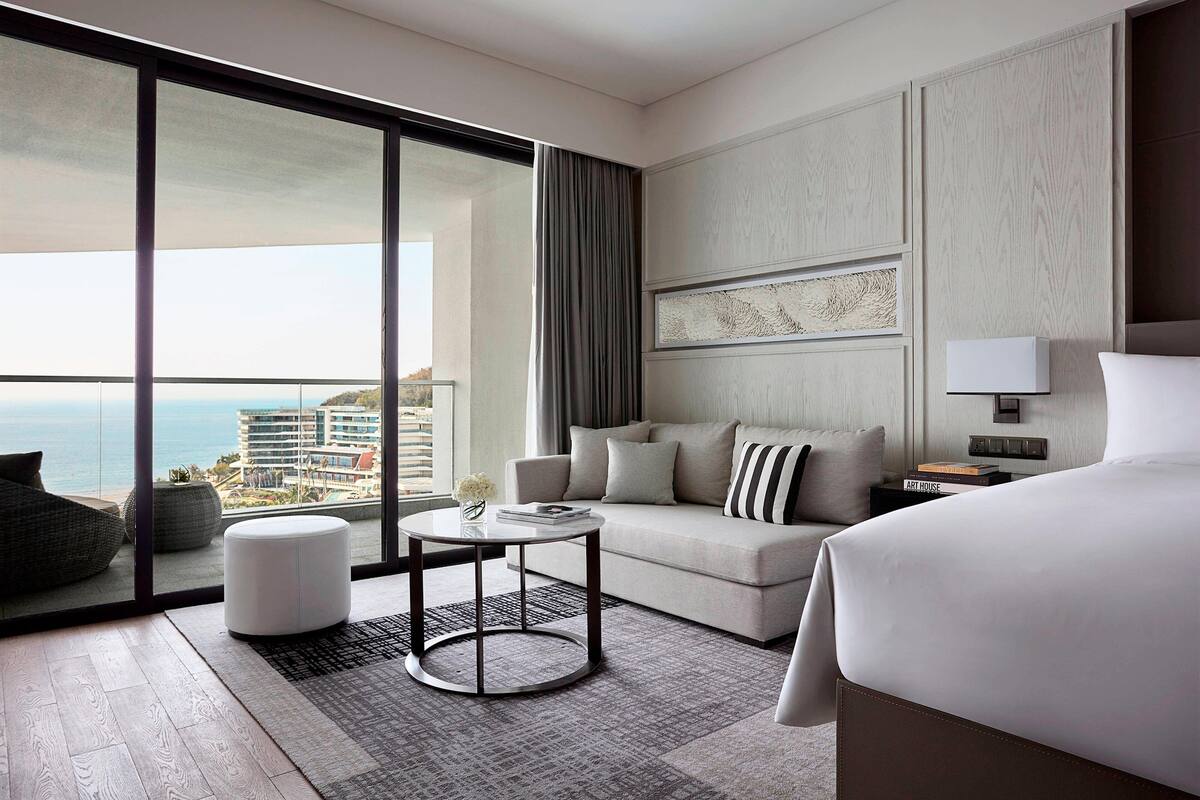 Une chambre d’hôtel moderne dotée d’un grand balcon, d’un canapé, d’une table basse ronde et d’un lit.