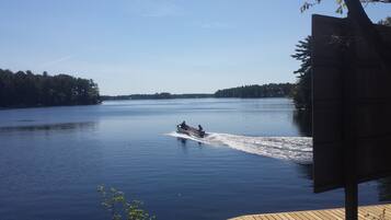 A boat speeding across a calm lake with a forested shoreline.