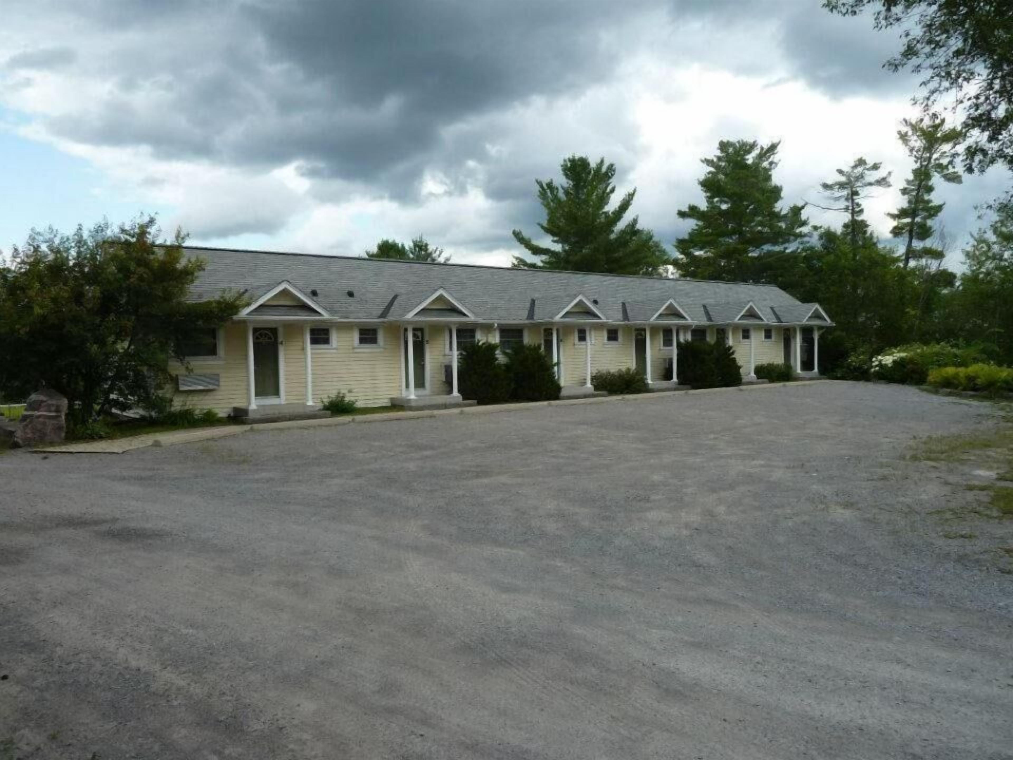 A motel with a row of single-story rooms, each with a front porch and a small attached garage.