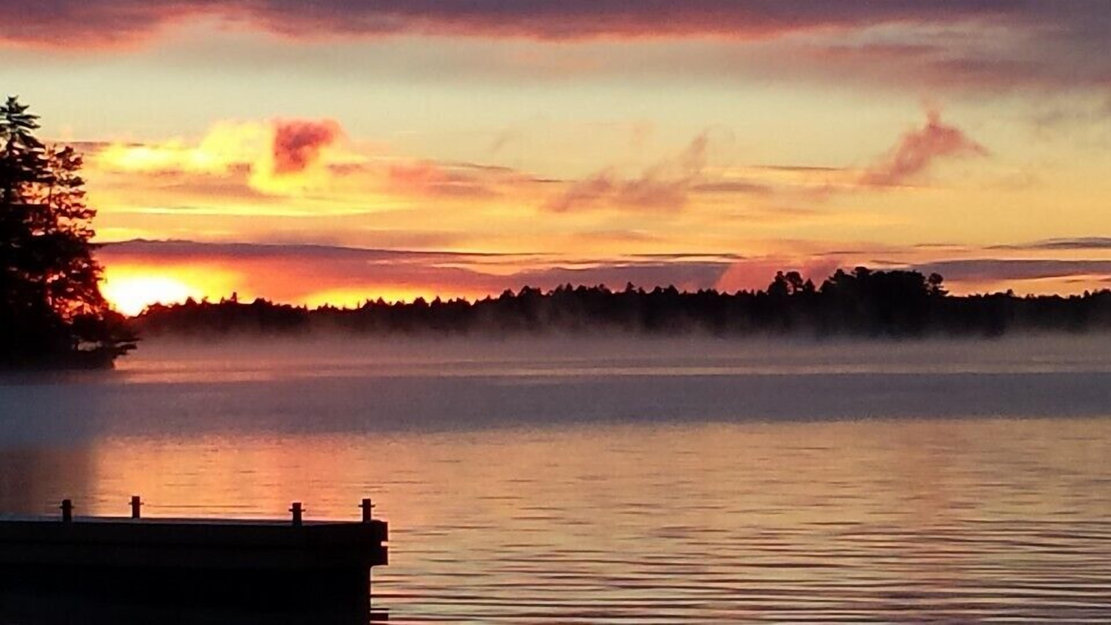 A calm lake at sunset with a dock in the foreground.