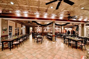 A spacious dining hall with high ceilings and ornate ceiling details, featuring multiple dining tables and chairs arranged for guests. - The Burleigh Falls Inn & Suites (North Kawartha)