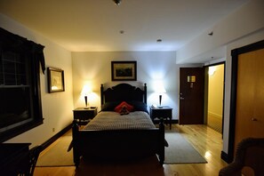 A bedroom with a bed, two bedside tables with lamps, a framed picture on the wall, and a door to another room. - The Burleigh Falls Inn & Suites (North Kawartha)