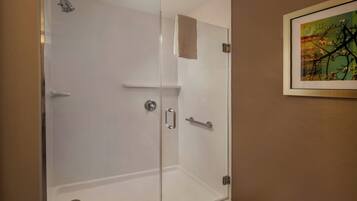 A glass-enclosed shower with a white door, a towel hanging on the wall, and a framed picture above it.