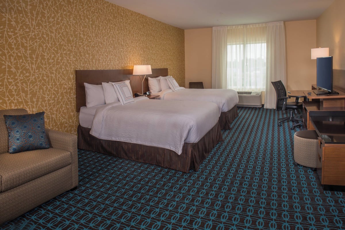 Ein Hotelzimmer mit zwei Betten, einem Schreibtisch, einem Sessel, einer Couch und einem gemusterten Teppich.