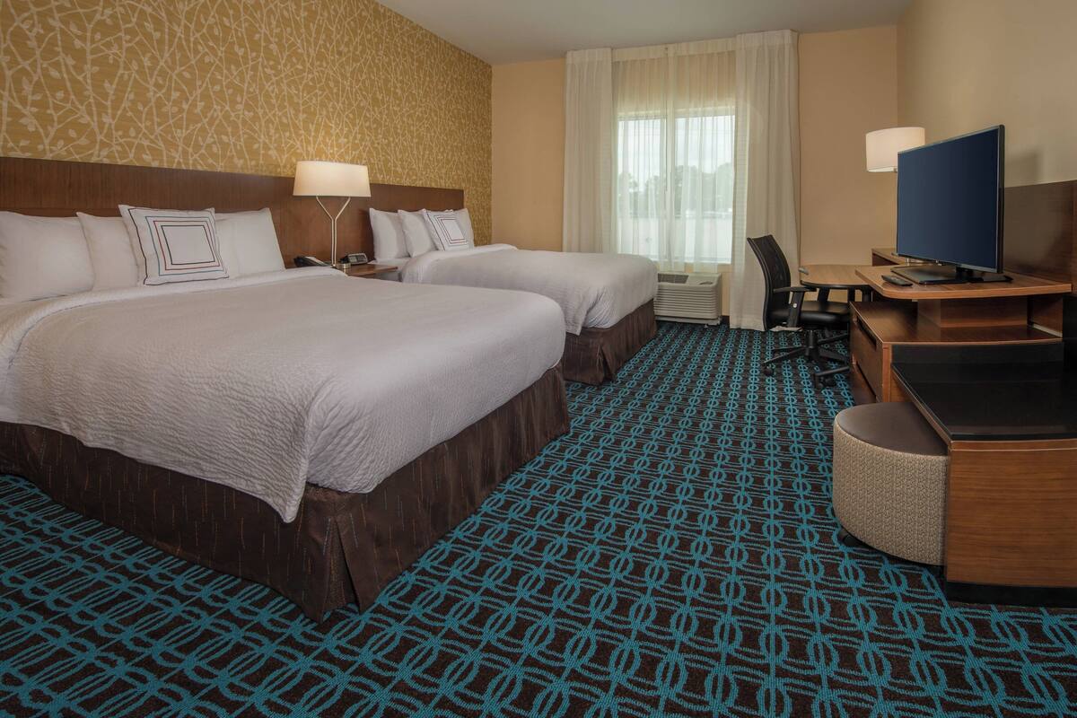 Ein Hotelzimmer mit zwei Betten, einem Schreibtisch, einem Computer, einem Stuhl und einem Fernseher.