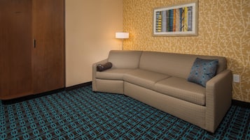 A corner room with a sofa, a patterned carpet, a wooden wardrobe, and a wall with a framed picture.