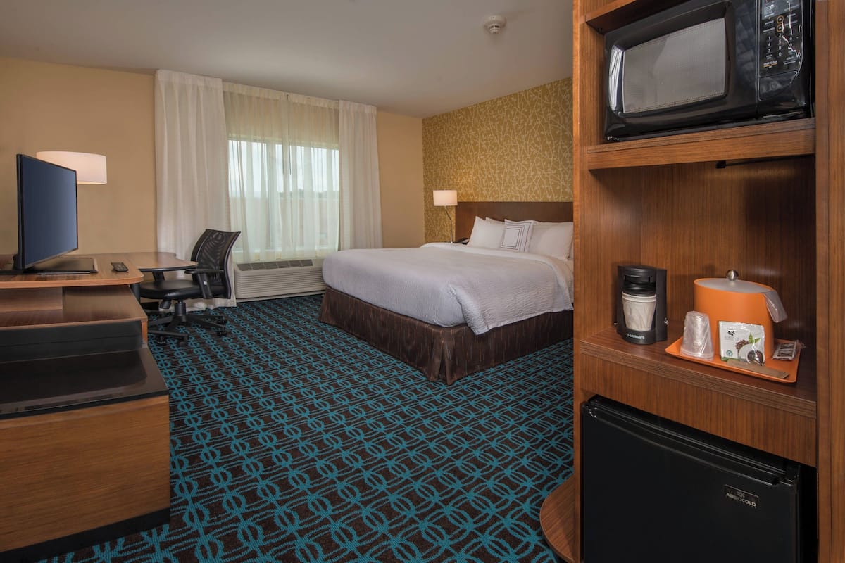 Ein Hotelzimmer mit einem Bett, einem Schreibtisch mit Computer, einem Fernseher, einer Mikrowelle und einem Kühlschrank.
