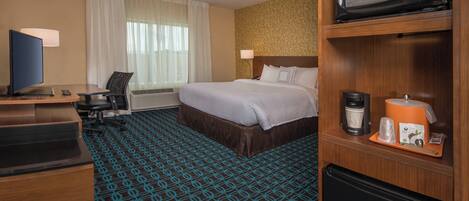 A hotel room with a bed, a desk with a computer, a television, a microwave, and a refrigerator.