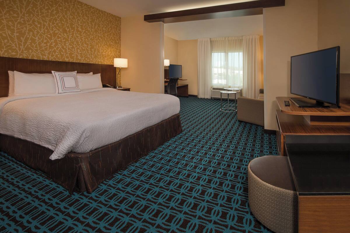 Ein Hotelzimmer mit einem großen Bett, einem Schreibtisch mit Computer, einem Fernseher und einer Sitzecke.
