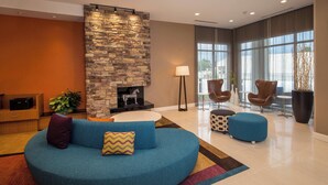 A modern lounge area with a stone fireplace, blue seating, and large windows. - Fairfield Inn and Suites by Marriott Washington (Washington)