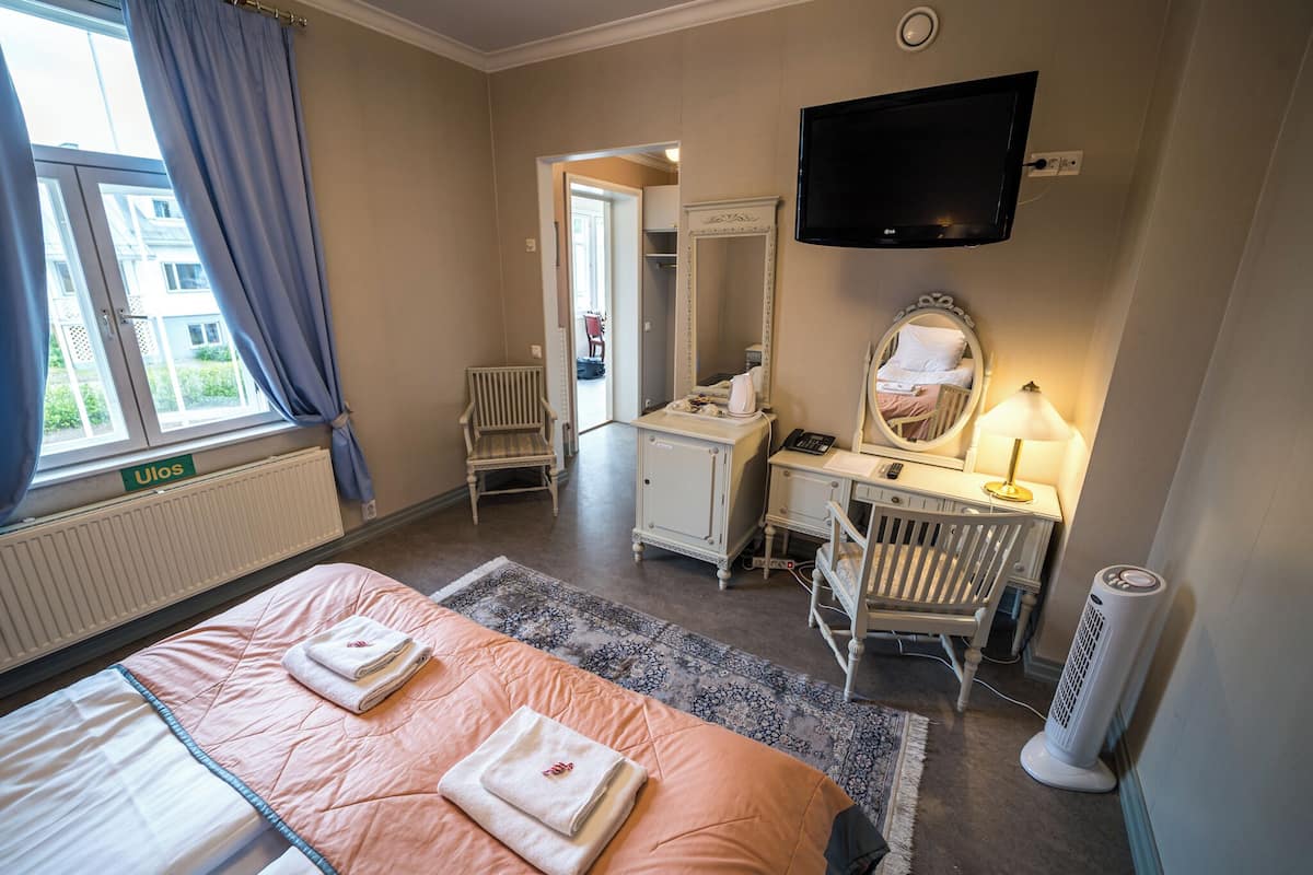 Een hotelkamer met een bed, bureau, stoel, spiegel, televisie en een radiator.