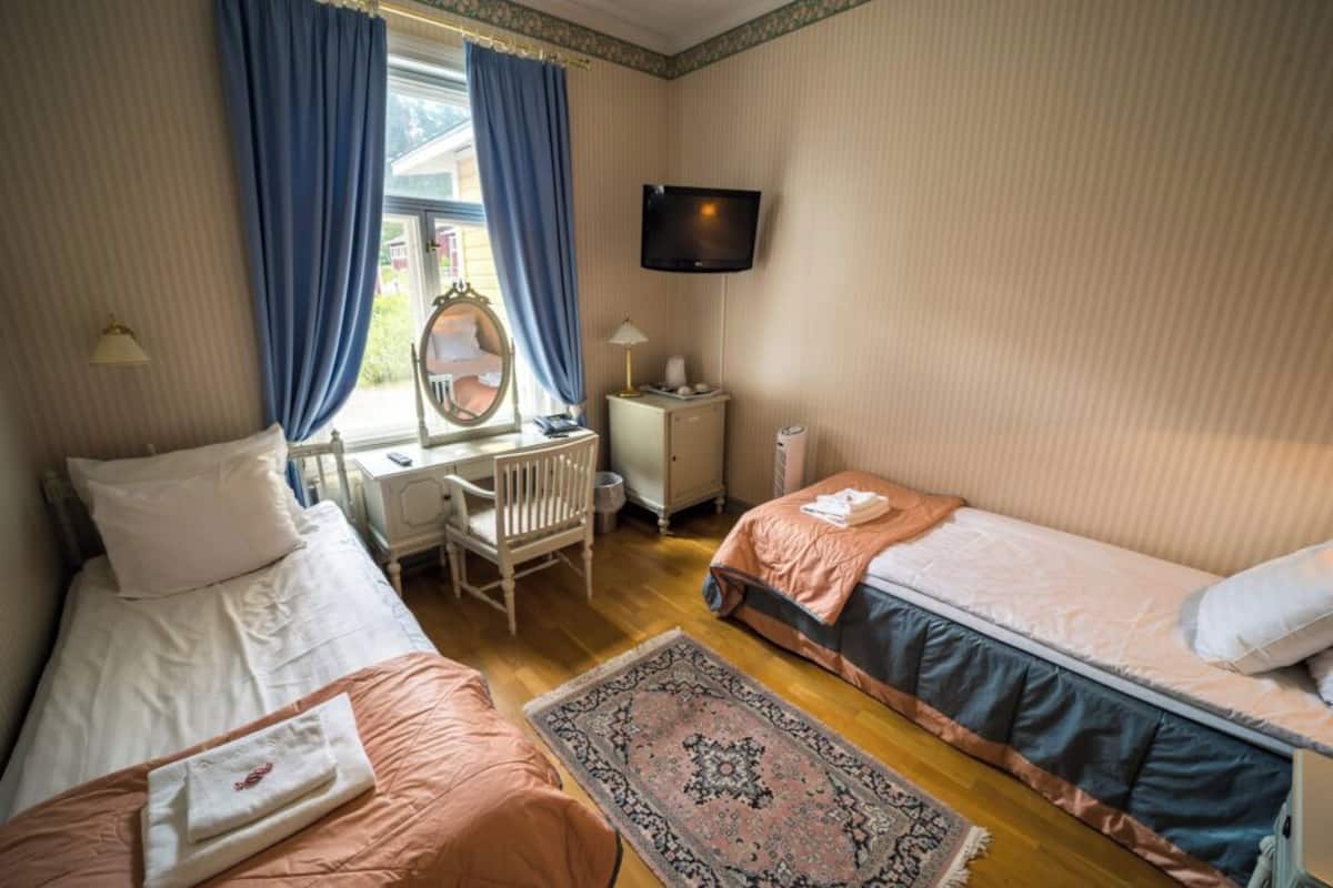 Een slaapkamer met twee bedden, een bureau, een stoel, een televisie en een raam met gordijnen.