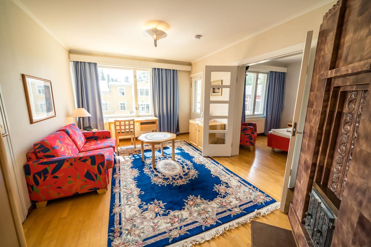 Een woonkamer met een bank, een klein tafeltje, een blauw gekleurd vloerkleed en een houten vloer.