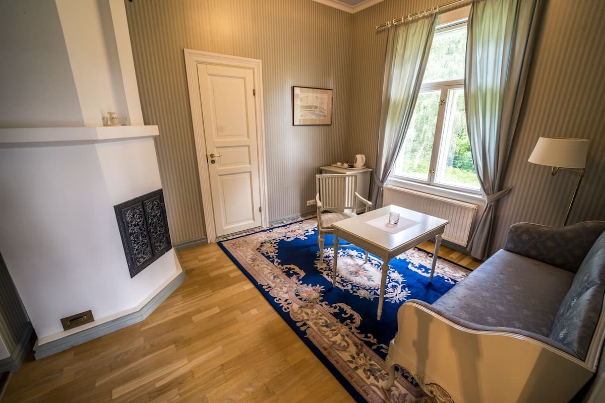Een kamer met een open haard, een tafel, een bank en een raam met gordijnen.