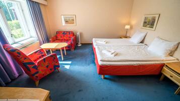 A hotel room with a bed, a chair, a table, and a window with curtains.