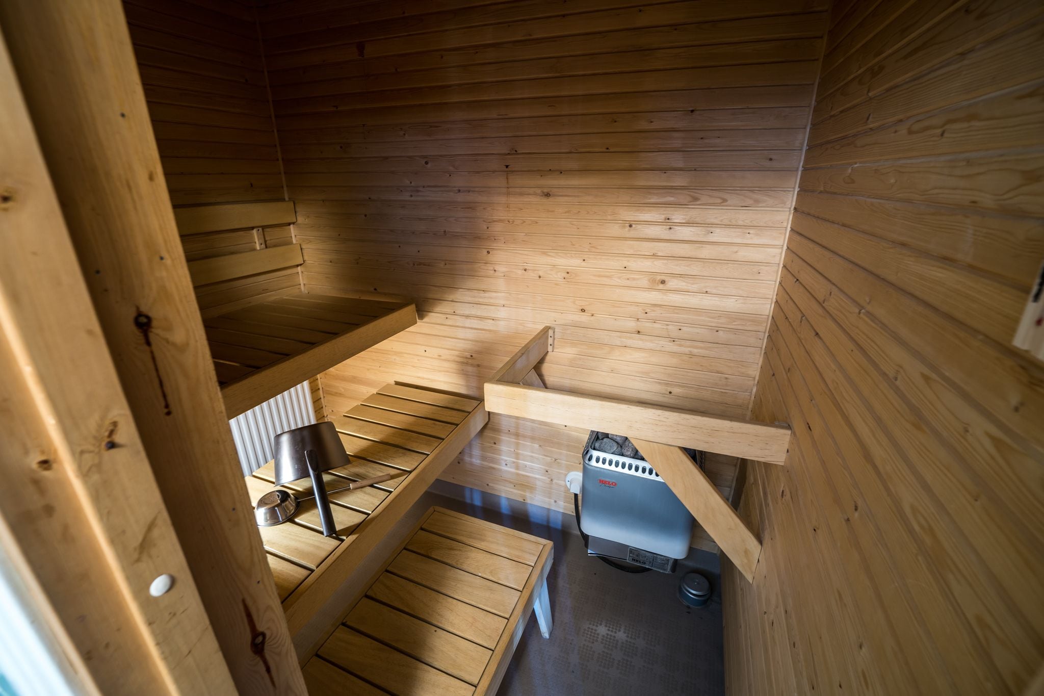 A wooden cabin interior with a wooden staircase, a heater, and a metal railing.