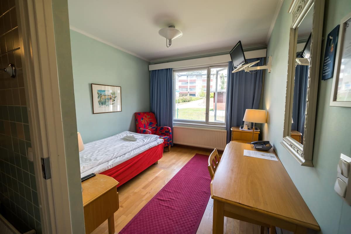 Een hotelkamer met een bed, een bureau, een stoel, een raam met gordijnen, een lamp en een spiegel.