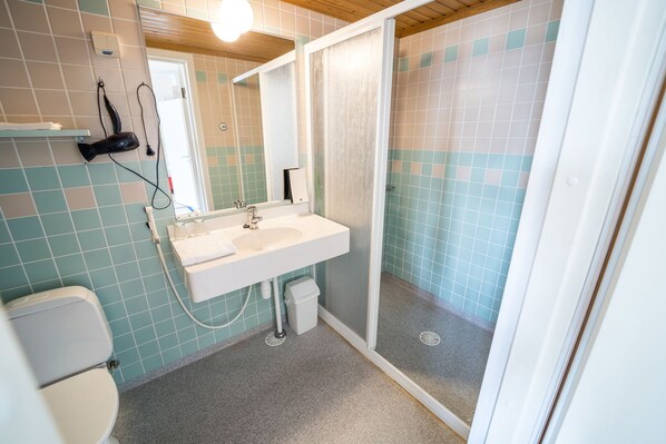 Baño con lavamanos blanco, espejo y cabina de ducha.