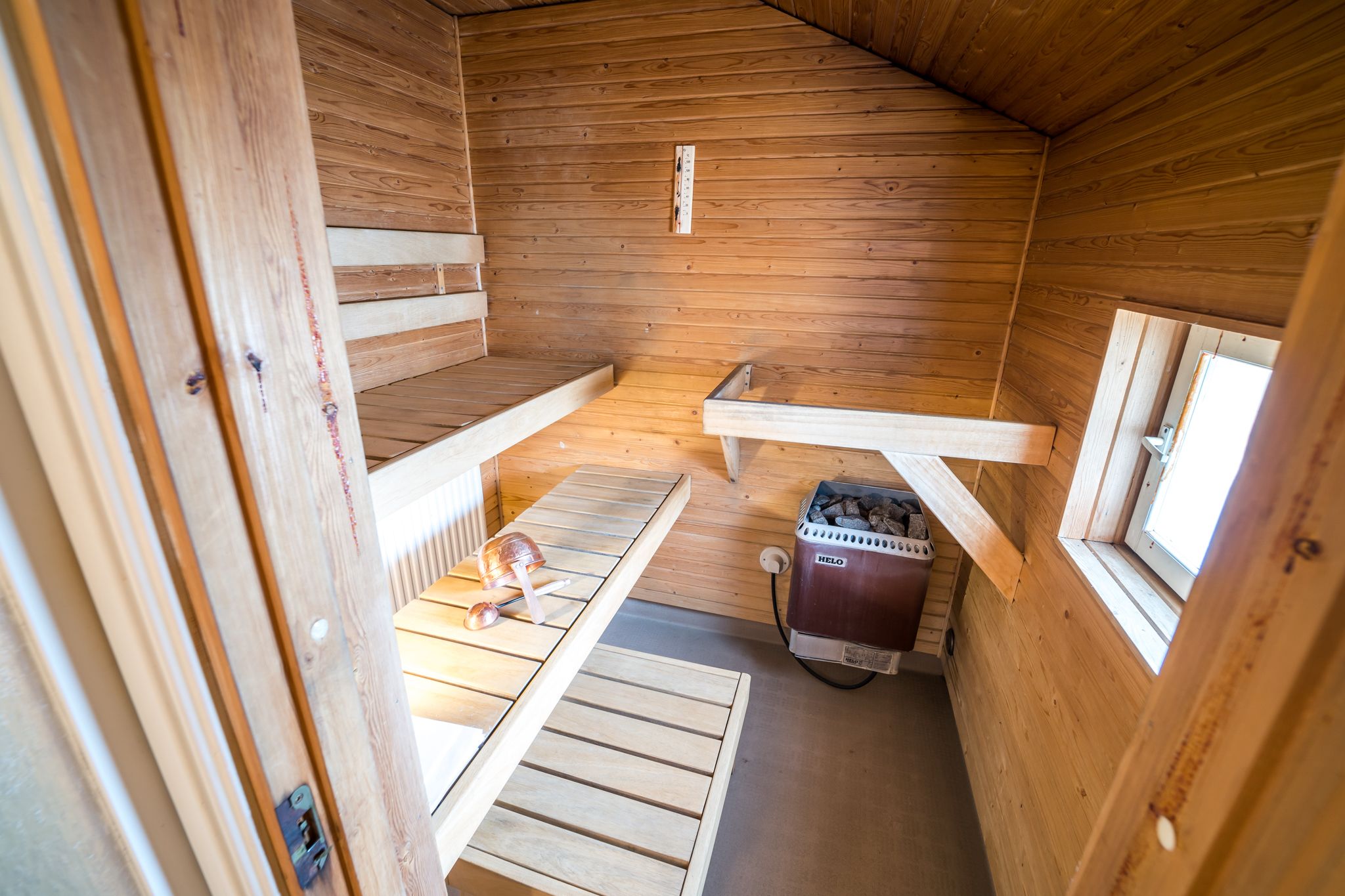A wooden cabin interior with a sloped ceiling, a built-in bench, a heater, and a window.