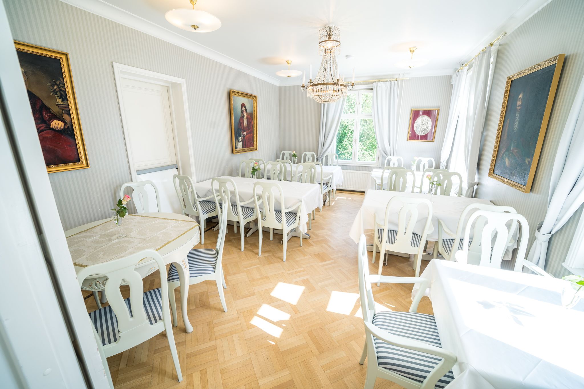 A dining area with white tables and chairs, a chandelier, and framed artwork on the walls.