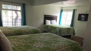 Habitación de hotel con dos camas, cada una con ropa de cama floral verde, cabeceros de madera y una ventana con cortinas.