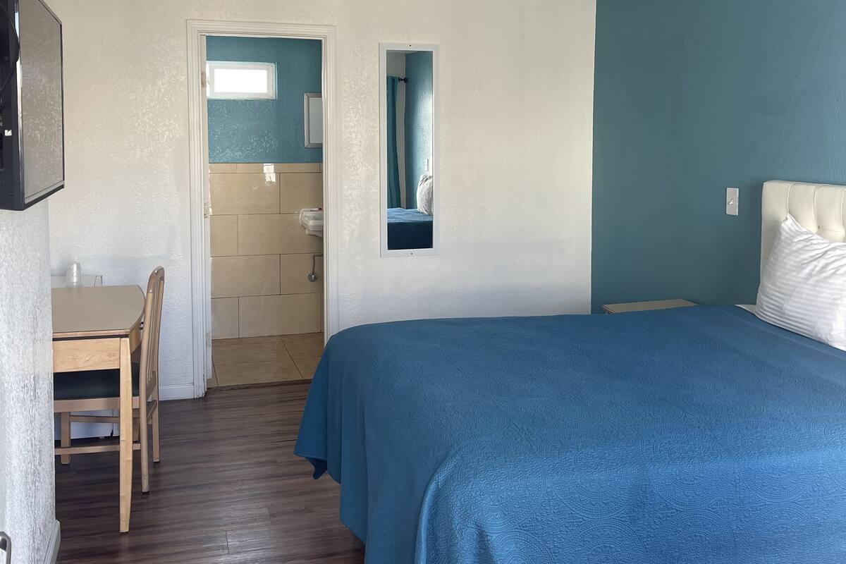 Un dormitorio con cama, escritorio y baño visible a través de una puerta abierta.