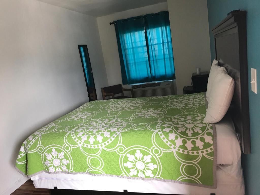 Un dormitorio con una cama, una ventana con cortinas, una mesita de noche y un espejo.